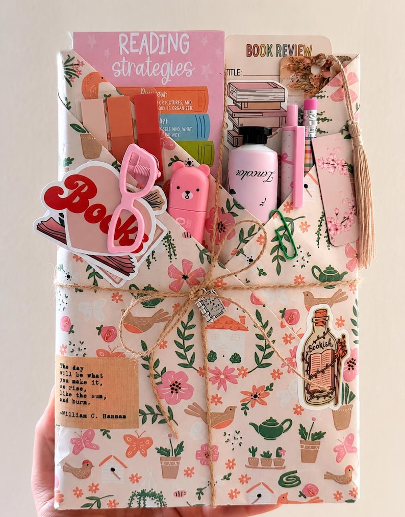 May include: A rectangular gift package wrapped in floral paper featuring birds, houses, and teapots. It contains a reading strategies card, a book review form, a pink bear-shaped highlighter, a pink pen, a pencil, and stickers including a book and a bottle.