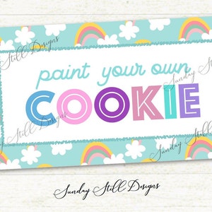 May include: A blue and white sign with a rainbow pattern and the text "paint your own cookie" in colourful letters.