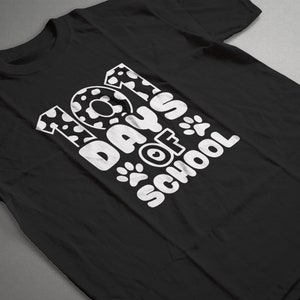 K&ouml;nnte beinhalten: Schwarzes T-Shirt mit wei&szlig;em Text, der "101 Tage Schule" lautet, mit Pfotenabdr&uuml;cken und einem Dalmatiner-Fleckenmuster auf den Zahlen.
