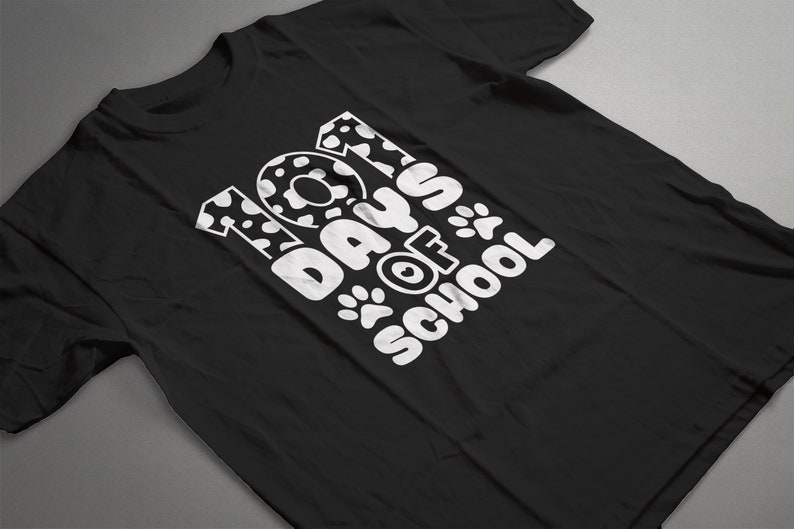 K&ouml;nnte beinhalten: Schwarzes T-Shirt mit wei&szlig;em Text, der "101 Tage Schule" lautet, mit Pfotenabdr&uuml;cken und einem Dalmatiner-Fleckenmuster auf den Zahlen.