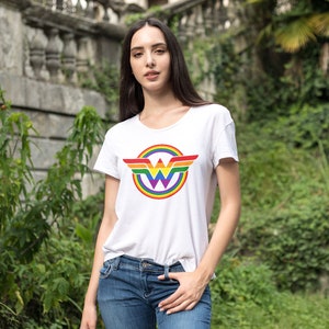 May include: A white t-shirt featuring a rainbow Wonder Woman logo. The logo is a circle with a rainbow design and the Wonder Woman symbol in the centre.