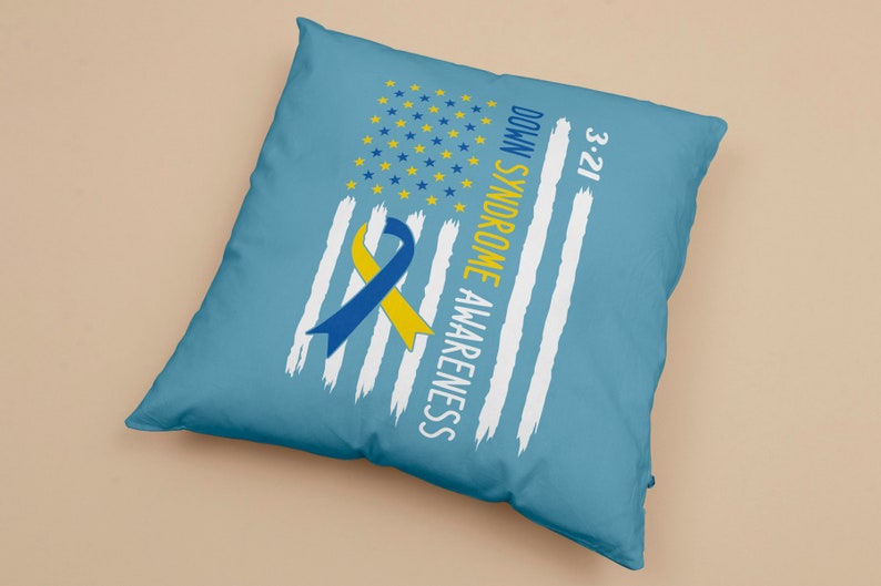 Może przedstawiać: Niebieska poduszka z białym wzorem amerykańskiej flagi i ż&oacute;łto-niebieską wstążką. Na poduszce nadrukowany jest tekst "Down Syndrome Awareness 3-21".