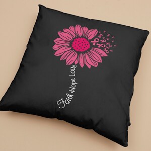 May include: Black pillow with a pink flower design and the text "Faith Hope Love" printed on the side. The flower is made up of pink ribbon symbols.