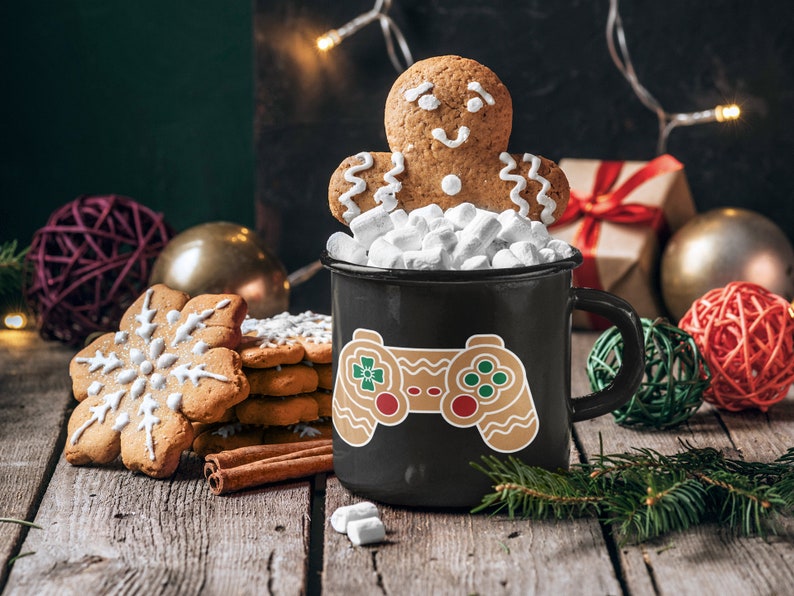 May include: A black mug with a gingerbread man controller design, filled with marshmallows and topped with a gingerbread man cookie. The mug is surrounded by Christmas decorations, including a gingerbread snowflake cookie, cinnamon sticks, and red and gold ornaments.
