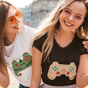 May include: Two friends wearing t-shirts with a Christmas-themed video game controller design. One shirt is white with a green and red controller, the other is black with a brown gingerbread controller.