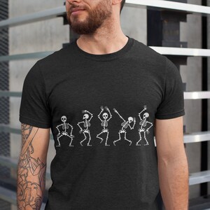May include: A black t-shirt with a graphic of five skeletons dancing. The skeletons are white and have a simple design.