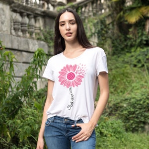 May include: White t-shirt with a pink sunflower design. The sunflower is made up of pink ribbon symbols. The text "Faith Hope Love" is written vertically on the stem of the sunflower.