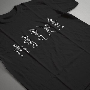 May include: Black t-shirt with a white graphic of five skeletons dancing. The skeletons are in different poses, with their arms and legs outstretched.
