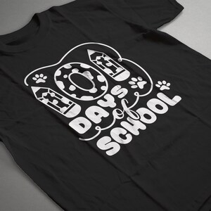 May include: Black t-shirt with white text that reads "100 Days of School" with a donut, paw prints, and pencils around the text.