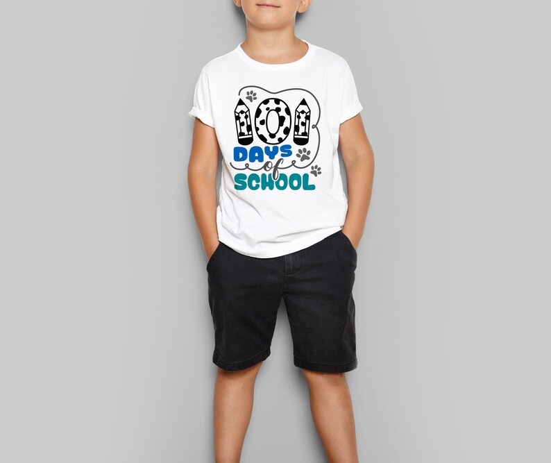 May include: A white t-shirt with a blue and black graphic that says "100 Days of School" with paw prints and pencils. The shirt is being worn by a child.