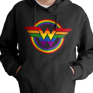 May include: A dark grey hoodie featuring a rainbow-coloured Wonder Woman logo. The logo is a circle with a rainbow around it and a stylised "W" inside.