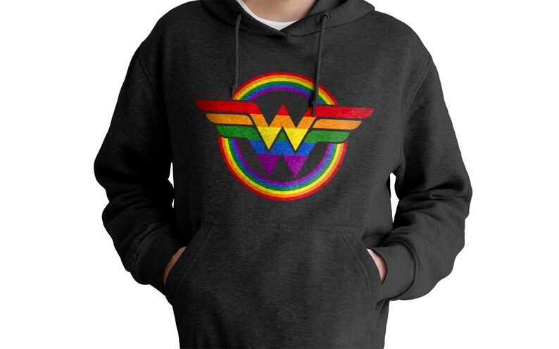 May include: A dark grey hoodie featuring a rainbow-coloured Wonder Woman logo. The logo is a circle with a rainbow around it and a stylised "W" inside.