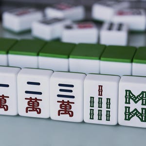 May include: Close-up of Mahjong tiles, a traditional Chinese game. The tiles are white with green and red markings. The image shows a selection of tiles with various symbols and characters.