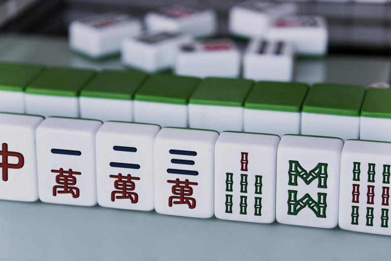 May include: Close-up of Mahjong tiles, a traditional Chinese game. The tiles are white with green and red markings. The image shows a selection of tiles with various symbols and characters.