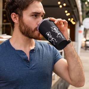 May include: A black travel mug with a white design of two skeletons dancing. The mug is made of stainless steel and has a clear lid.