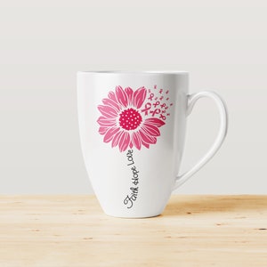 May include: White ceramic coffee mug with a pink sunflower design. The sunflower has pink ribbon designs around it. The text "Faith Hope Love" is written vertically on the mug.