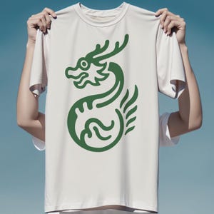 May include: A white t-shirt featuring a green dragon design. The dragon is stylized with curved lines and a detailed head, set against a plain background. The shirt has a crew neck and short sleeves.