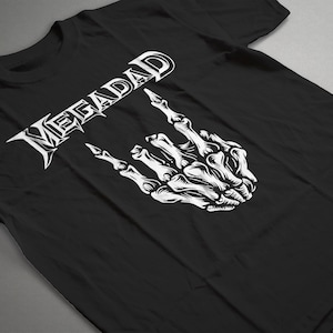 Może przedstawiać: Czarny T-shirt z białym nadrukiem słowa "Megadeth" w stylizowanym foncie i szkieletową ręką wykonującą gest rock and roll.