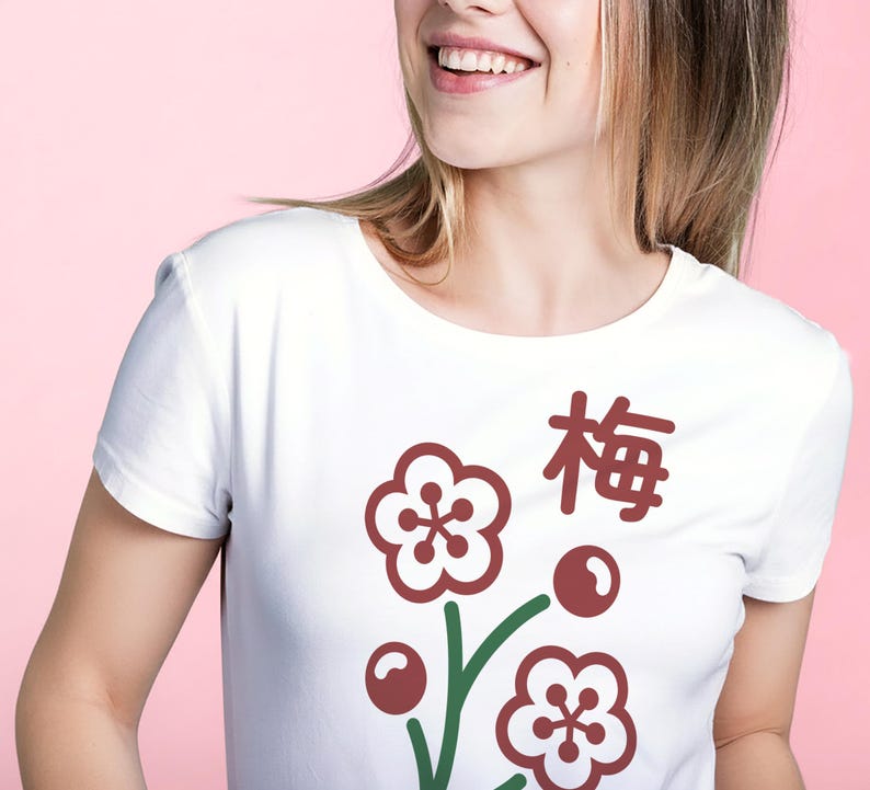 May include: White t-shirt featuring a floral design with the Japanese character for plum. The design includes maroon flowers, berries, and green stems. The shirt is a classic crew neck style.