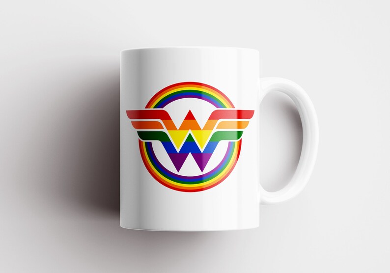 May include: White ceramic mug featuring a rainbow-coloured Wonder Woman logo. The logo depicts a stylised "W" with wings and a rainbow circle surrounding it.