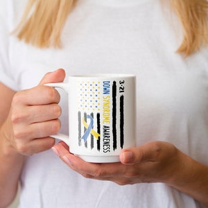 Może przedstawiać: Biały kubek ceramiczny z niebieską i ż&oacute;łtą wstążką i tekstem "Down Syndrome Awareness 3-21" na czarno-białym wzorze amerykańskiej flagi.