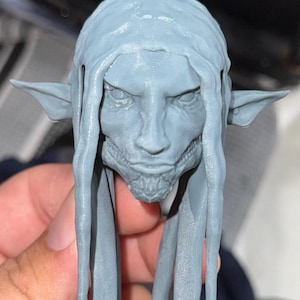 May include: A 3D printed gray figurine of a creature with long hair, pointed ears, and a menacing expression.