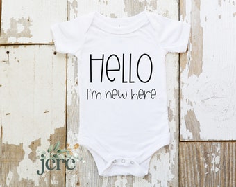 May include: White baby onesie with black text that reads "Hello I'm new here".
