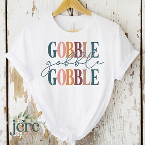 May include: White t-shirt with the text "GOBBLE gobble GOBBLE" in stacked, colorful lettering. The text is in shades of pink, orange, brown, and teal.