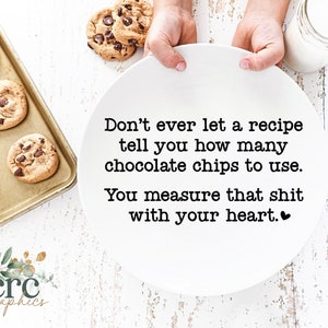May include: White ceramic plate with the text "Don't ever let a recipe tell you how many chocolate chips to use. You measure that shit with your heart." A heart symbol is at the end of the text. A tray of chocolate chip cookies is in the background.