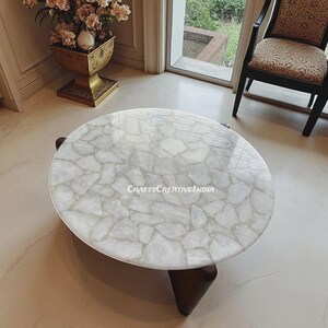 May include: An oval coffee table featuring a white mosaic top and dark brown legs. The table's surface has a glossy finish and a distinctive pattern. This decorative furniture piece is suitable for a living room or lounge area, with a diameter of approximately 100 cm.