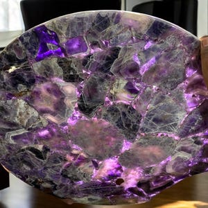Könnte beinhalten: Eine runde, violette Amethyst-Tischplatte aus vielen kleinen Amethyst-Stücken. Die Tischplatte wird von unten beleuchtet, wodurch der Amethyst leuchtet.