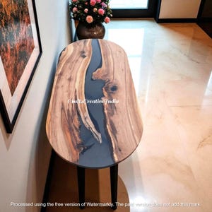 May include: A wooden side table with a dark gray epoxy resin river design. The table has a natural wood grain finish and black legs. The text "CraftsCreative India" is visible on the table's surface.