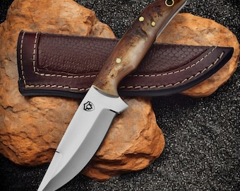 May include: A brown and white handled knife with a stainless steel blade. The knife has a leather sheath with stitching around the edges.