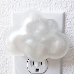 May include: A white cloud-shaped nightlight plugged into a standard electrical outlet.