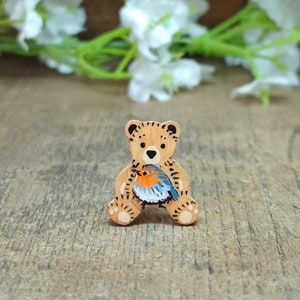 May include: A wooden bear figurine painted with brown fur and holding a blue and orange robin in its arms.