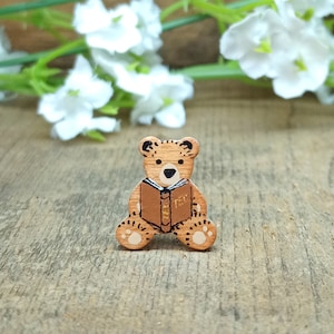 May include: A wooden bear figurine sitting on a wooden surface. The bear is brown and has a book in its paws. The book is brown and has gold lettering that says "The Book".