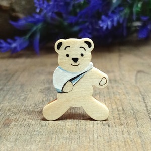 May include: A wooden bear figurine with a light blue bandage on its arm. The bear is painted with a light brown body and a white face. The bear is standing on a wooden surface.