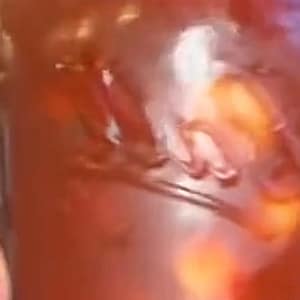 May include: A close-up of a glass jar filled with a reddish-orange liquid and visible chunks. The jar has a wide mouth and a slight curve. The contents appear to be a food item, possibly a sauce or preserve.