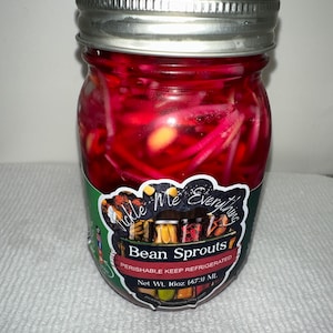 May include: A glass jar filled with pickled bean sprouts. The jar has a silver lid and a label that reads "Tickle Me Everything Bean Sprouts." The contents are a vibrant red color. The net weight is 16oz (473 mL).