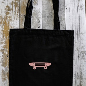 Op de afbeelding: Zwarte tote bag met een roze skateboard ontwerp.