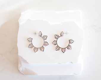 May include: A pair of silver hoop earrings with a geometric design. The earrings are made of metal and have a shiny finish.