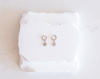 May include: A pair of silver hoop earrings with a star charm hanging from each hoop.