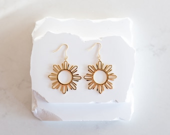 May include: A pair of gold earrings with a sun design. The earrings are on a white background.