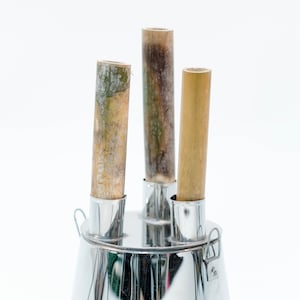 May include: Three bamboo sticks are inserted into a silver metal holder. The sticks are different lengths and have a natural brown color.
