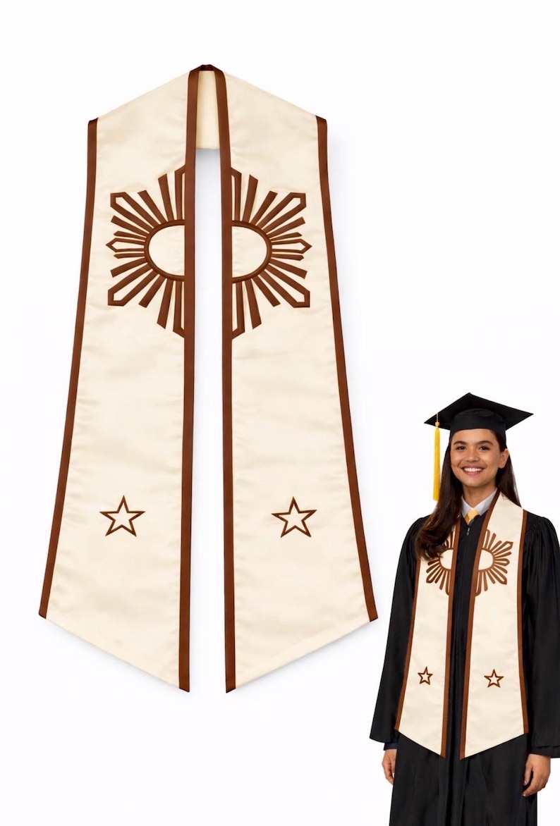 May include: Cream-colored graduation stole with brown trim and sunburst and star designs. The stole is worn by a person in a black graduation gown and cap. The stole is a symbol of academic achievement.