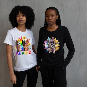 Könnte beinhalten: Zwei Personen tragen Grafik-T-Shirts. Eines ist ein weißes T-Shirt mit einem Regenbogen-Design von Händen in Gebärdensprache, Sonnenblumen und den Worten "BE KIND". Das andere ist ein schwarzes Langarmshirt mit einem Sonnenblumen-Design und den Worten "Be Kind".