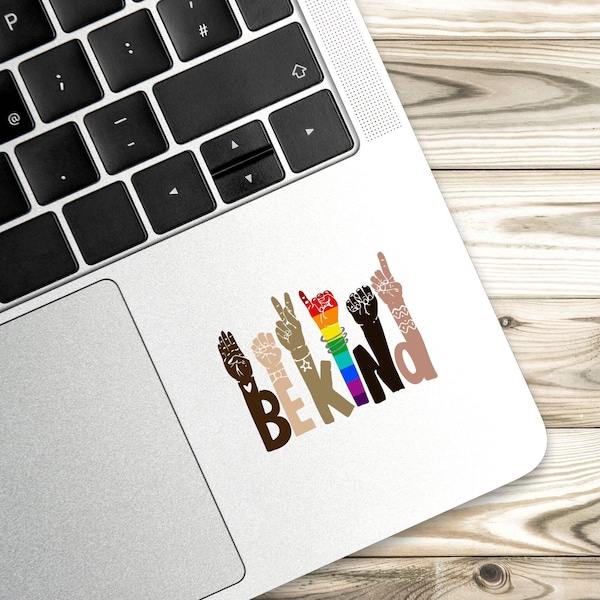 Puede incluir: Una pegatina con un diseño de arcoíris que dice "Be Kind" en letras negras. El diseño presenta múltiples manos en diferentes tonos de piel, cada una haciendo un gesto diferente.