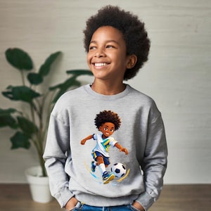 Pode incluir: Um moletom cinza com uma ilustração de desenho animado de um jogador de futebol chutando uma bola de futebol. O jogador está usando um uniforme branco, azul e amarelo. O moletom é feito de um material macio.