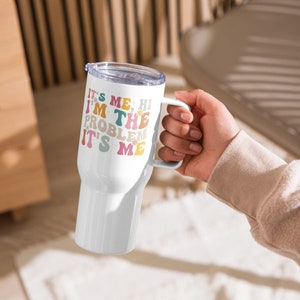 May include: White stainless steel travel mug with a colourful graphic that reads "It's me, hi I'm the problem it's me".