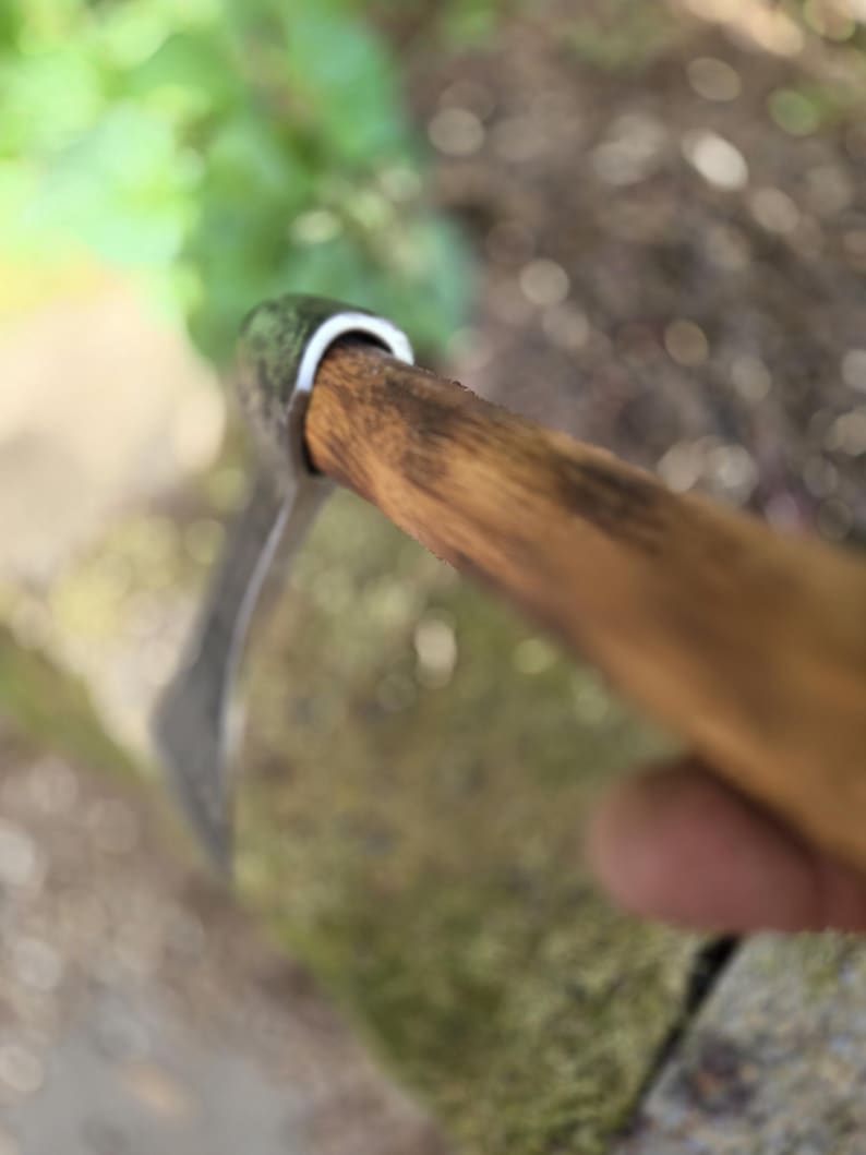 Op de afbeelding: Close-up van een tuinhark met een houten steel en een metalen blad. De steel is lichtbruin van kleur en het blad is zilver. De tool is ontworpen voor tuin- en landschapstaken.